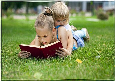 Girl reading a story with her sister on the grass